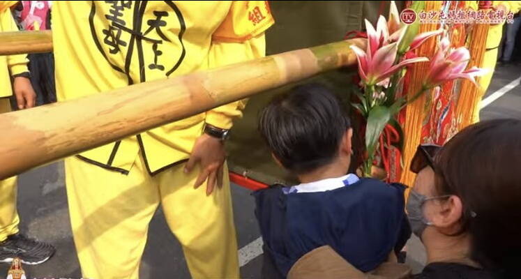 依偎在媽媽懷裡的小男童在鑾轎前面接受媽祖的洗禮與賜福。(圖擷取白沙屯媽直播) 依偎在媽媽懷裡的小男童在鑾轎前面接受媽祖的洗禮與賜福。(圖擷取白沙屯媽直播)